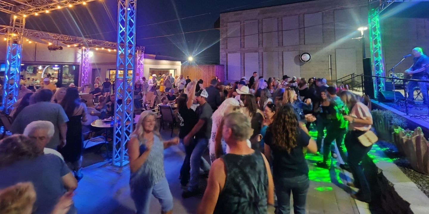 A packed outdoor dance floor under truss lighting with Ron performing on stage