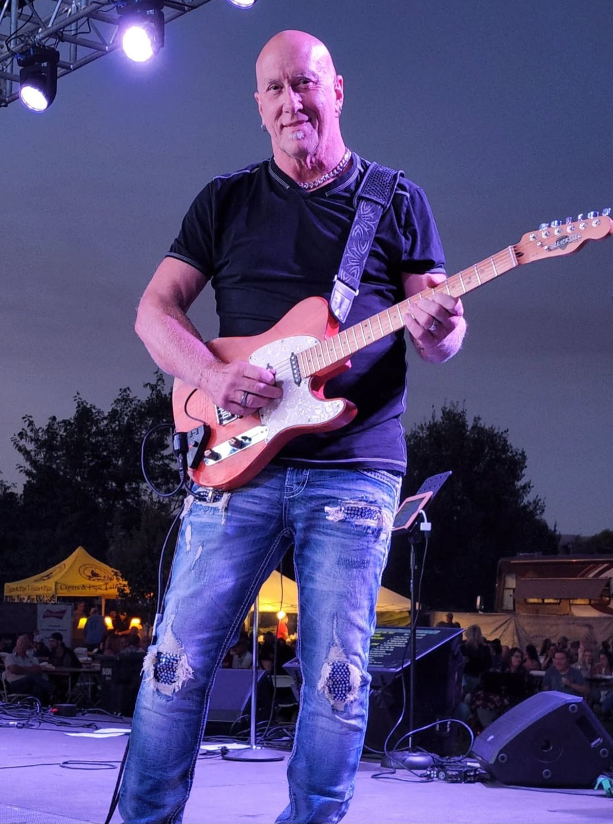 Ron Mears on an outdoor stage at night playing a sparkle-top electric guitar under purple stage lights